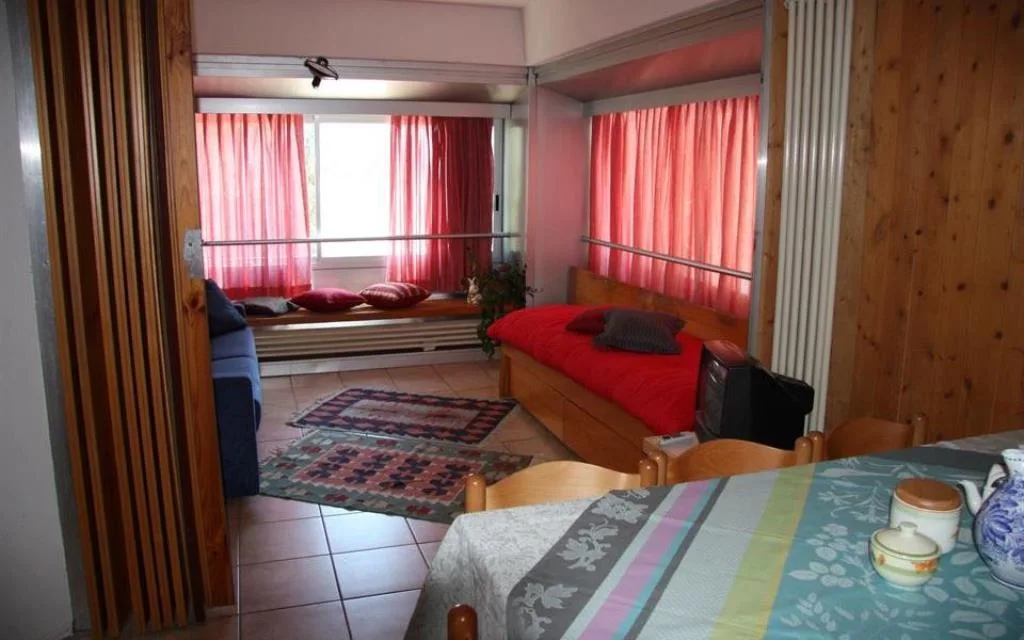 Camera luminosa con letto, divano, tende rosse e tavolo da pranzo apparecchiato