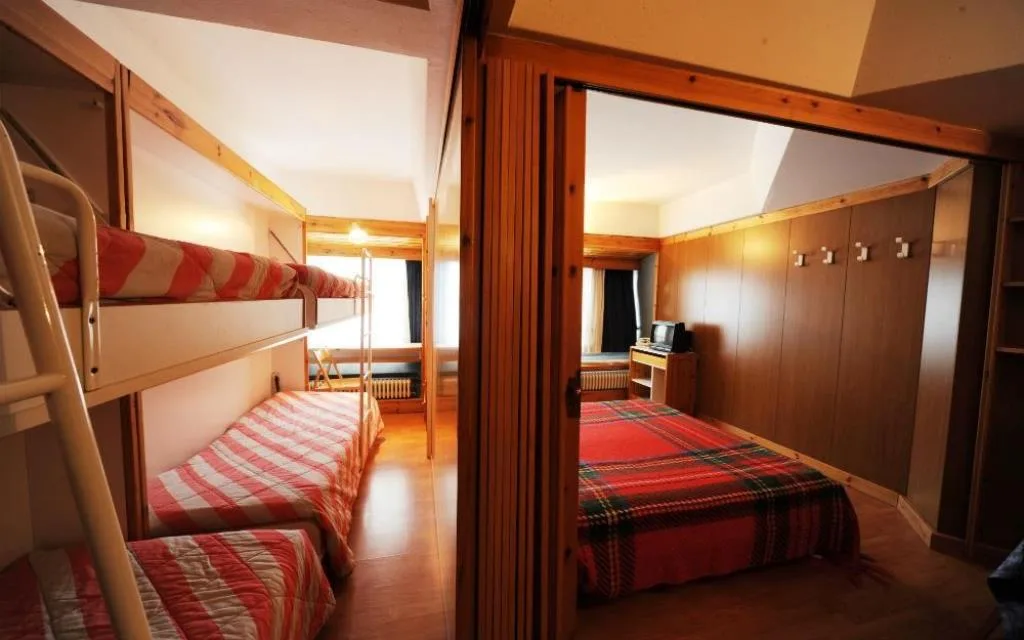 Camera con letto a castello e letto singolo, armadiature in legno e pareti rivestite in legno