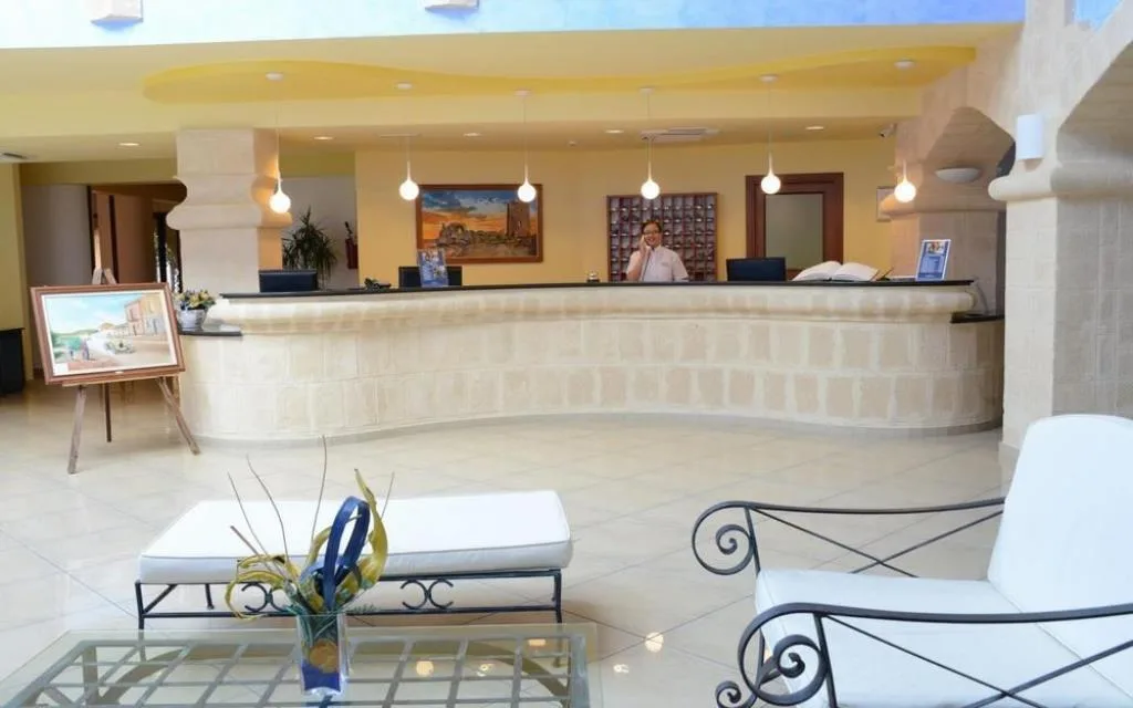 Reception dell'hotel con bancone in pietra, poltrone bianche e addetto al telefono