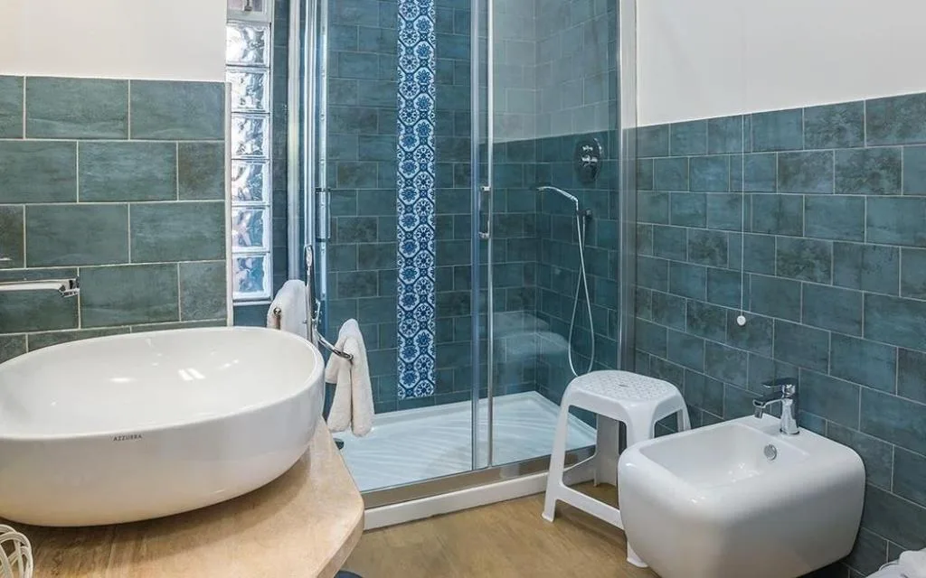 Bagno con piastrelle azzurre decorate, doccia, lavabo tondo e bidet