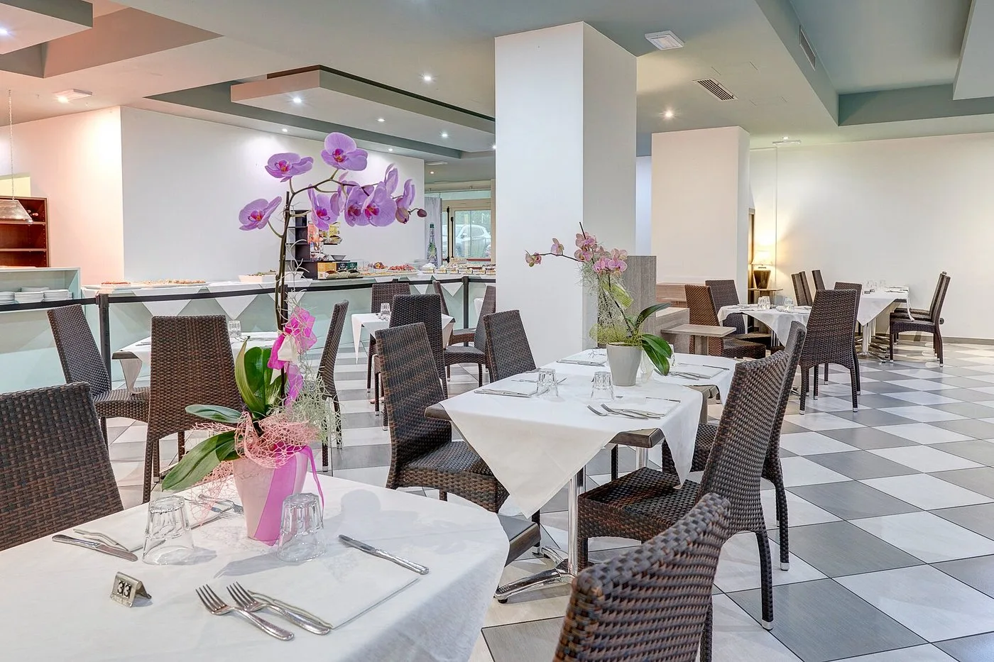 Sala ristorante moderna con tavoli apparecchiati, decorazioni floreali e zona buffet