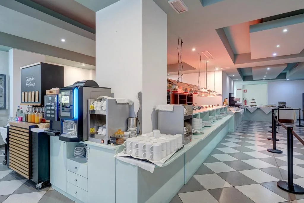 Area buffet con macchina del caffè, bevande e stoviglie disposte lungo il banco