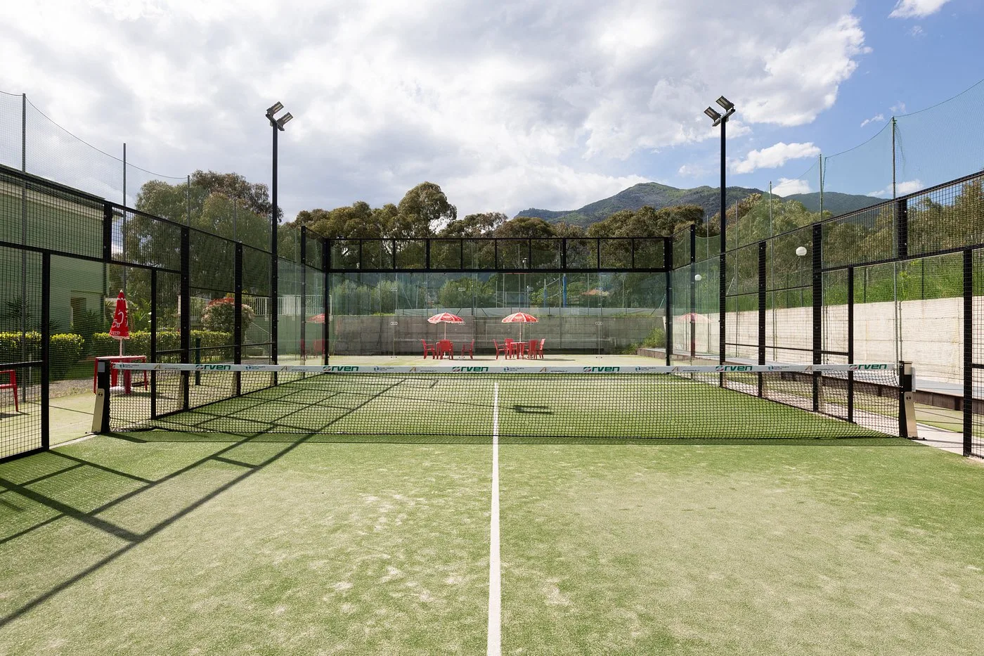Campo da padel con erba sintetica, recinzione in vetro e vista sulle montagne