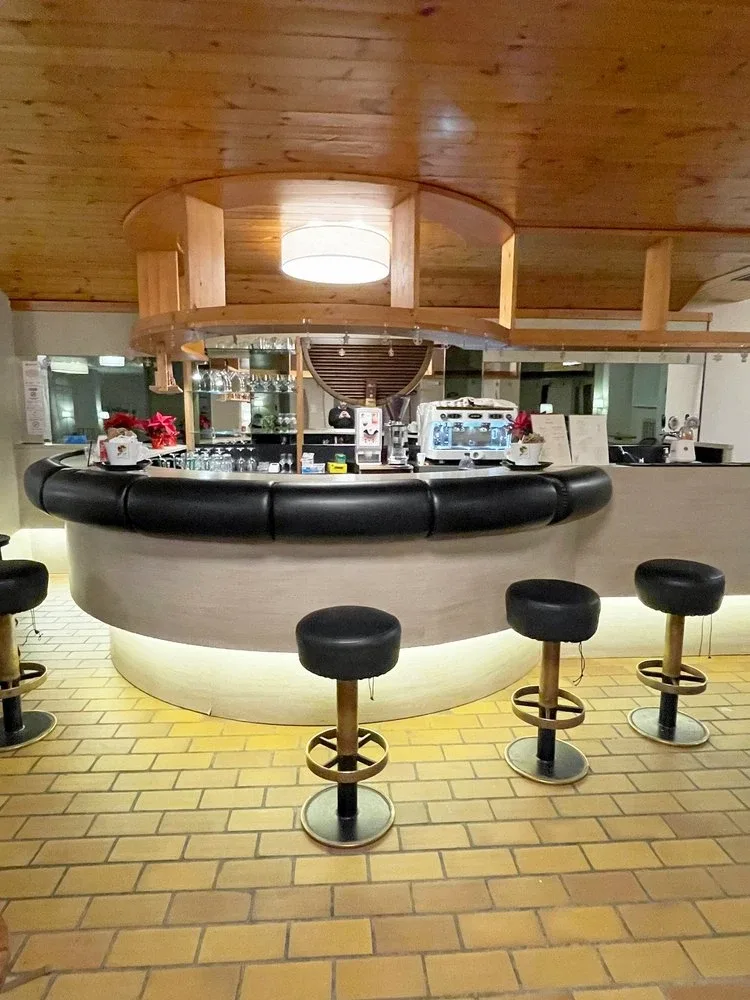 Bar circolare con sgabelli neri e controsoffitto in legno nella zona lounge dell'hotel