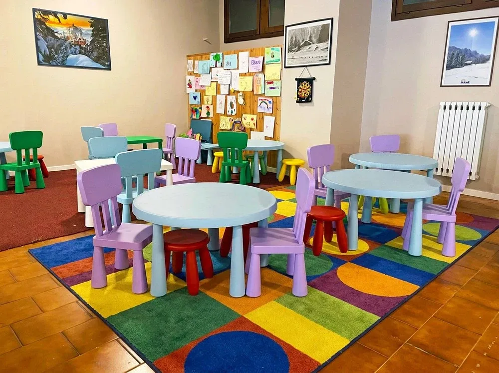 Sala giochi per bambini con tavolini colorati, sedie in plastica e tappeto multicolore