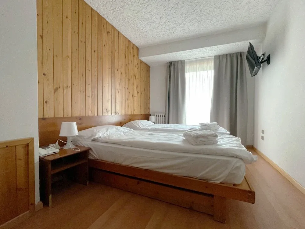 Camera matrimoniale semplice con testiera in legno, parquet chiaro e finestra