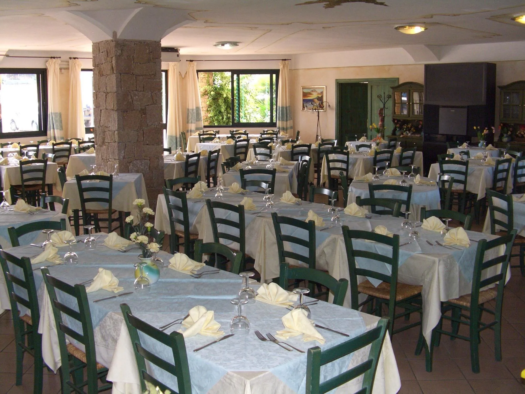 Sala ristorante interna con tavoli apparecchiati con tovaglie azzurre, sedie verdi e colonna centrale in pietra