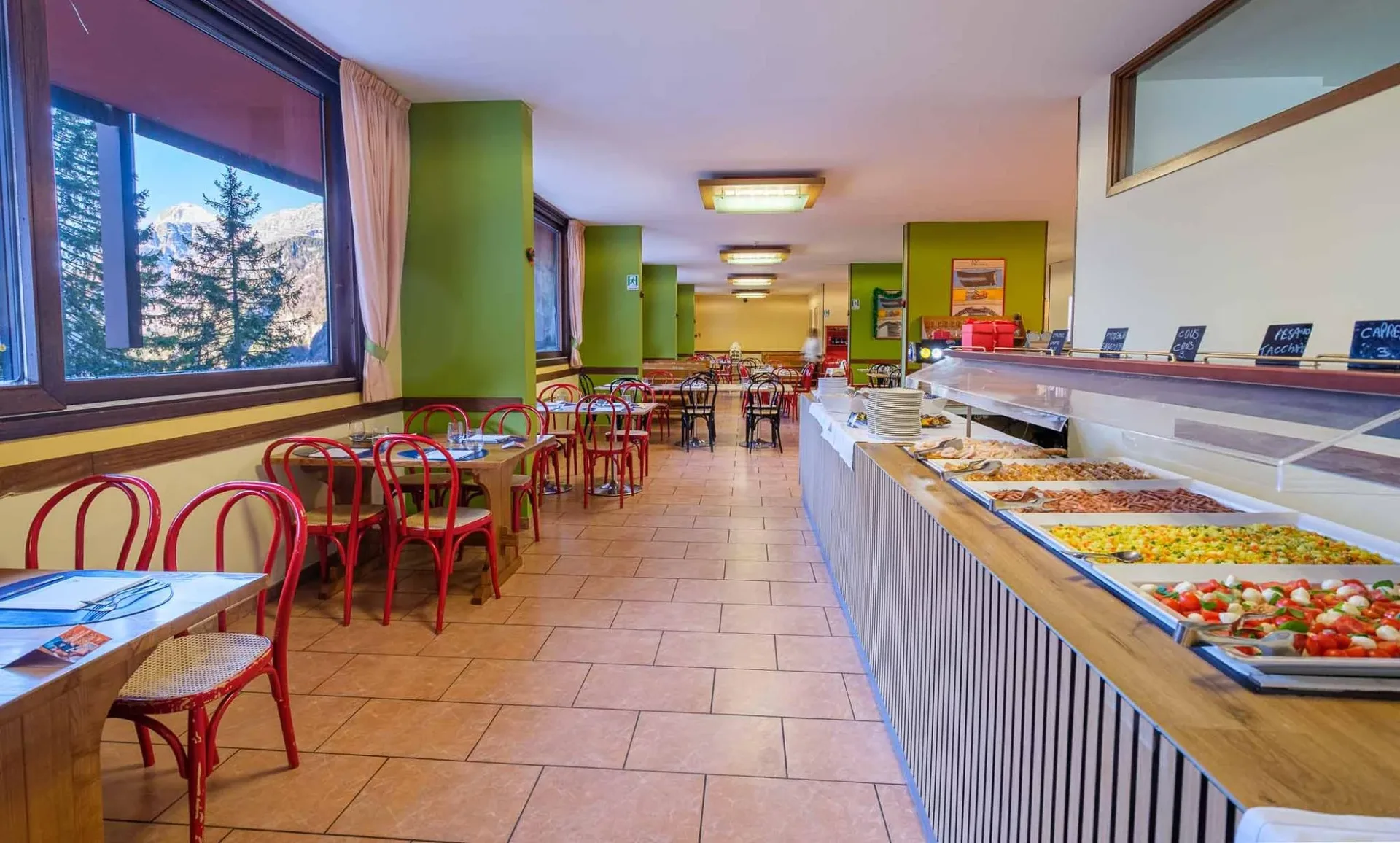 Sala ristorante con buffet e tavoli con sedie rosse e vista montagna