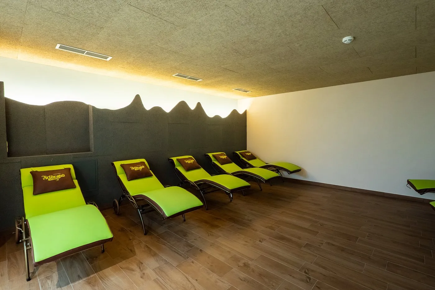 Sala relax con lettini verdi e parete sagomata a motivo montano