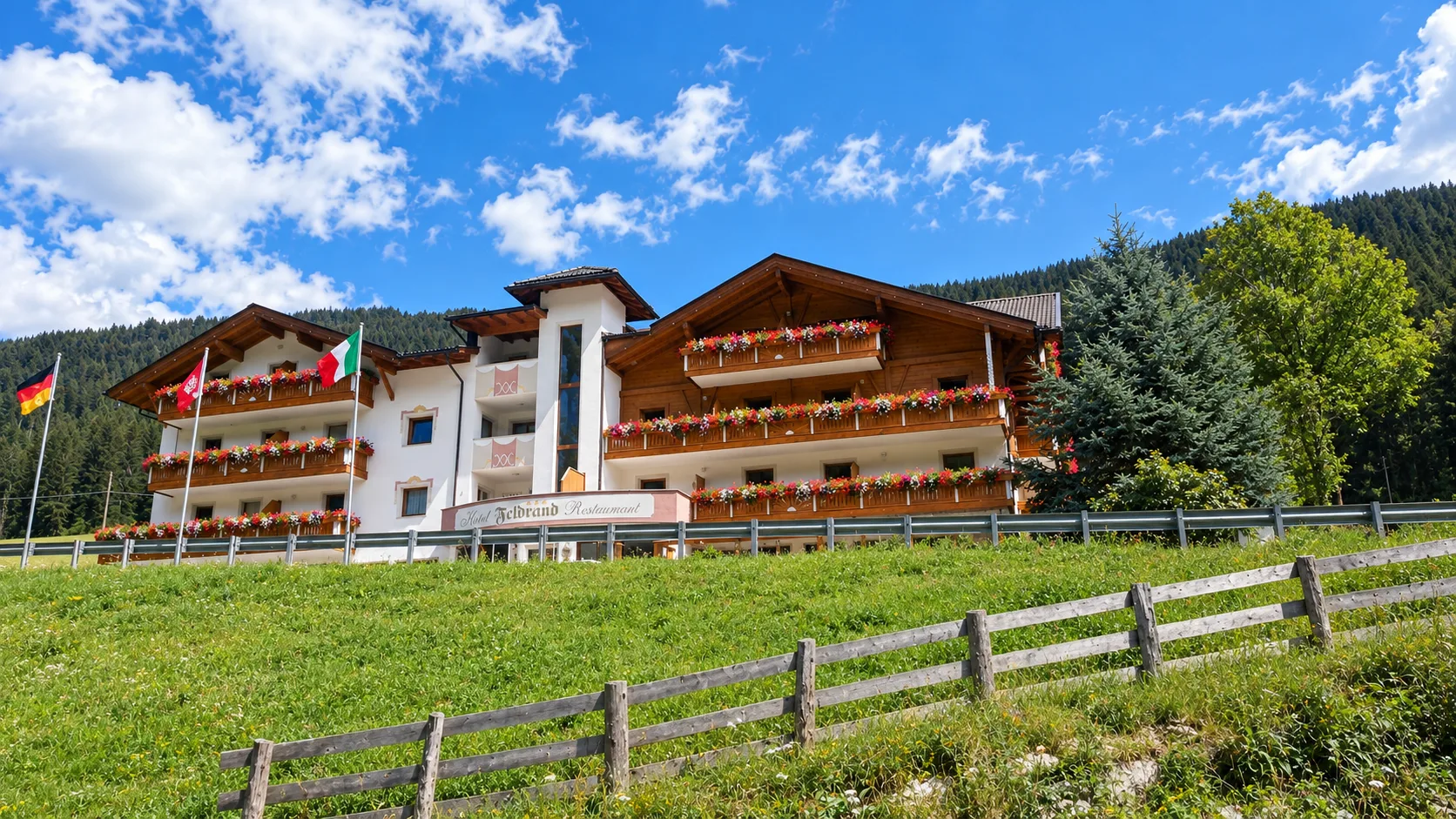 Facciata estiva dell'hotel con balconi fioriti, bandiere e prato verde