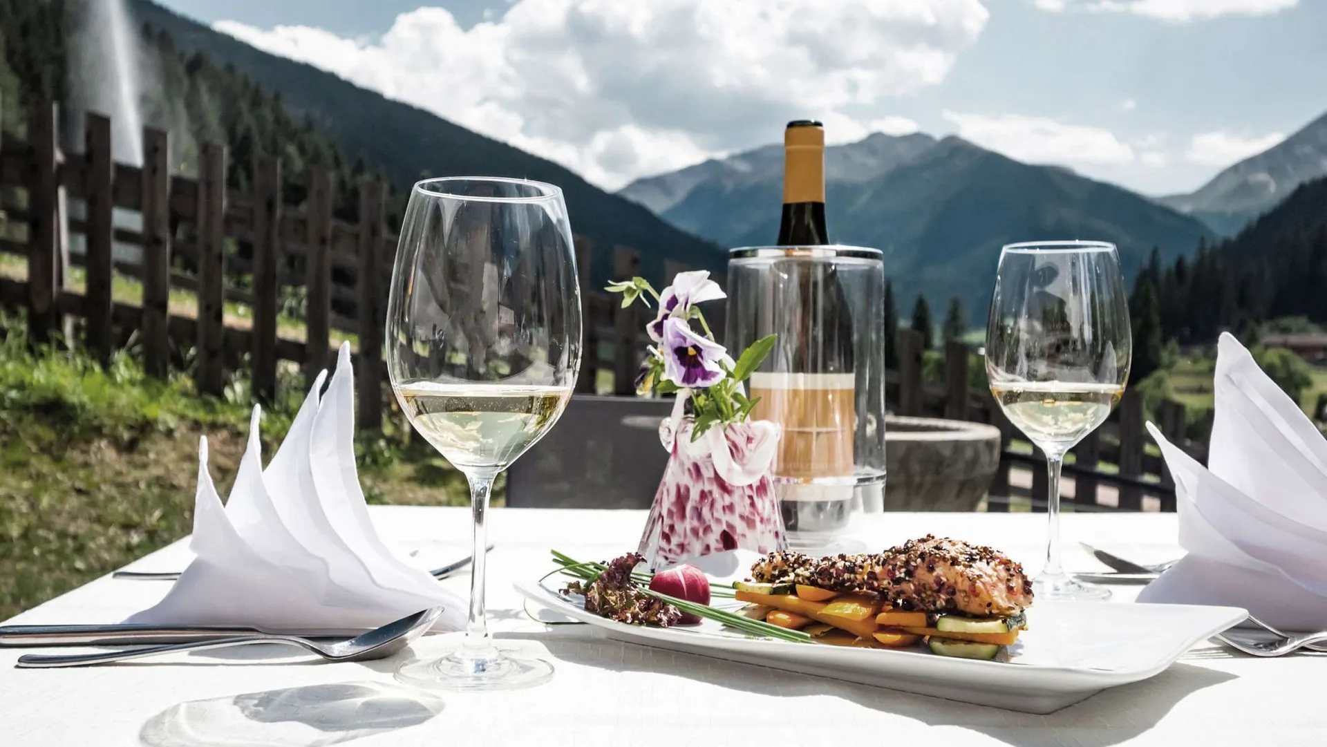 Piatto gourmet e vino bianco su tavolo in terrazza con vista sulle montagne