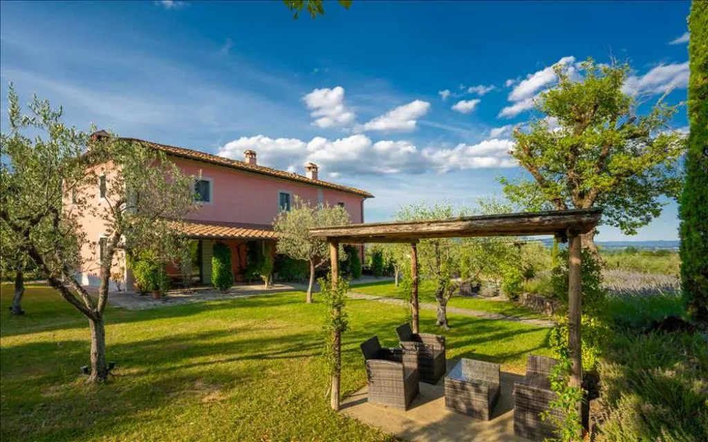 Villa toscana rosa con pergolato in legno e salottino esterno nel giardino con ulivi