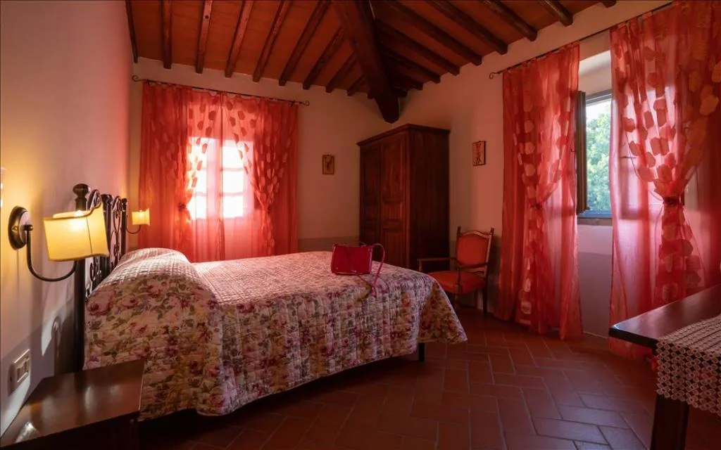 Camera da letto rustica con travi in legno, letto in ferro battuto e tende rosse