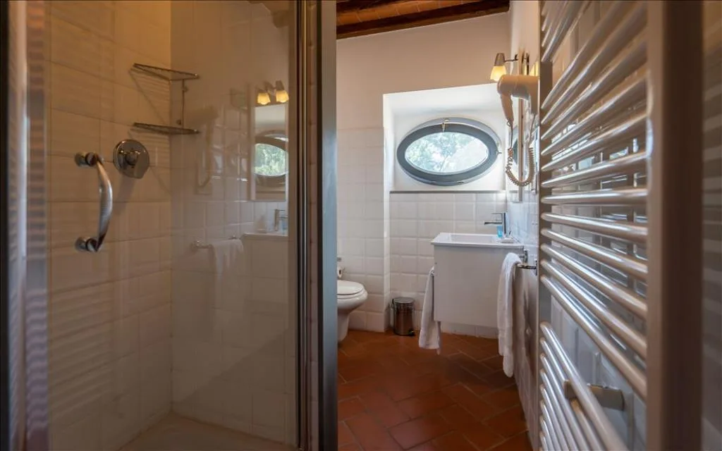Bagno con doccia, scaldasalviette, lavabo e finestra ovale affacciata sul verde