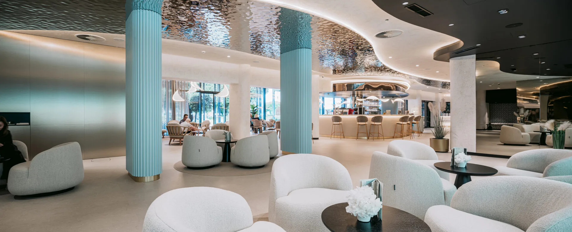 Lobby elegante con colonne azzurre, poltrone bianche e bar sullo sfondo