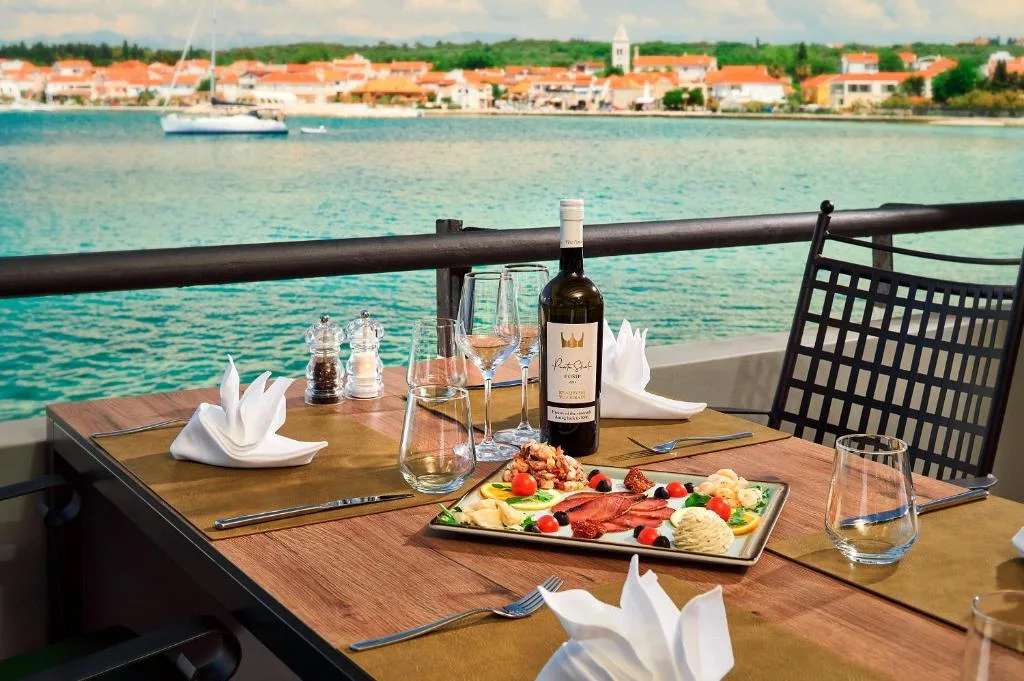 Tavolo apparecchiato con piatto di antipasti e vino affacciato sul mare e il borgo