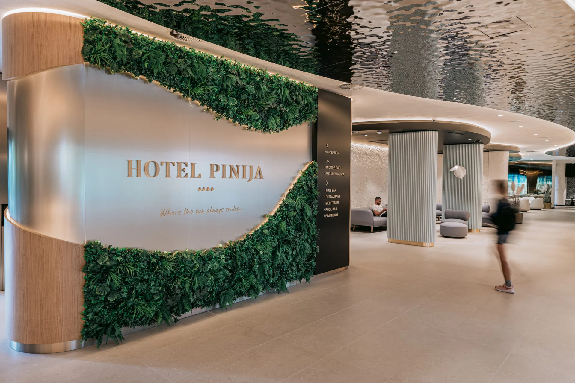 Ingresso dell'Hotel Pinija con parete verde verticale e insegna dorata