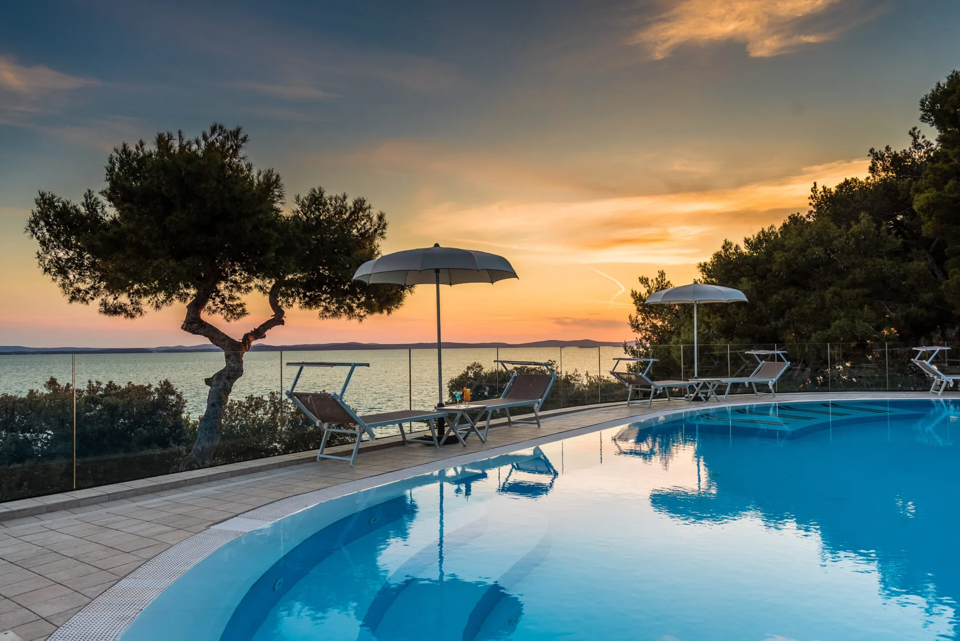 Piscina esterna con ombrelloni e lettini al tramonto con vista sul mare