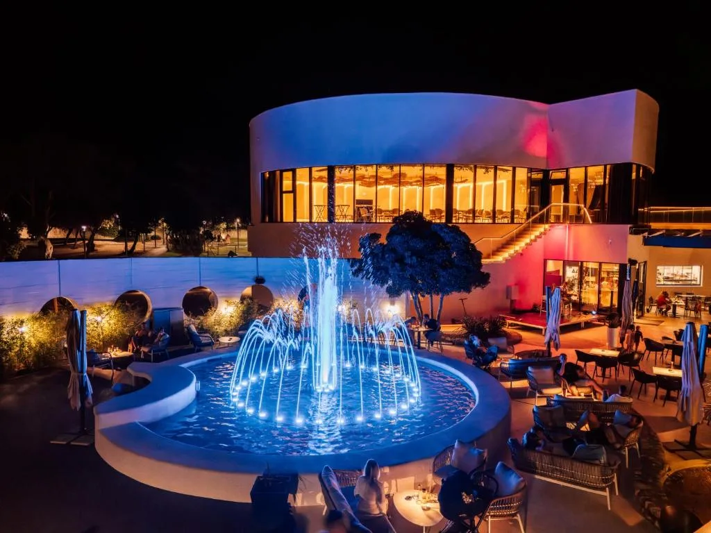 Edificio dell'hotel illuminato di notte con fontana giochi d'acqua e dehors