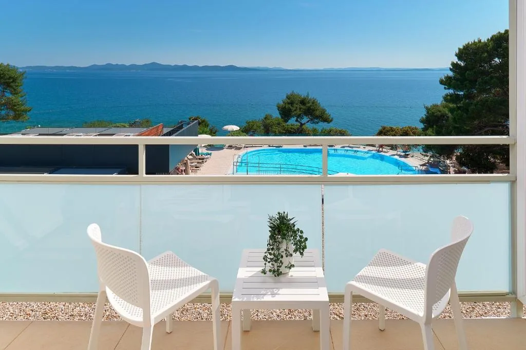 Balcone con tavolino e sedie bianche affacciato sulla piscina e il mare