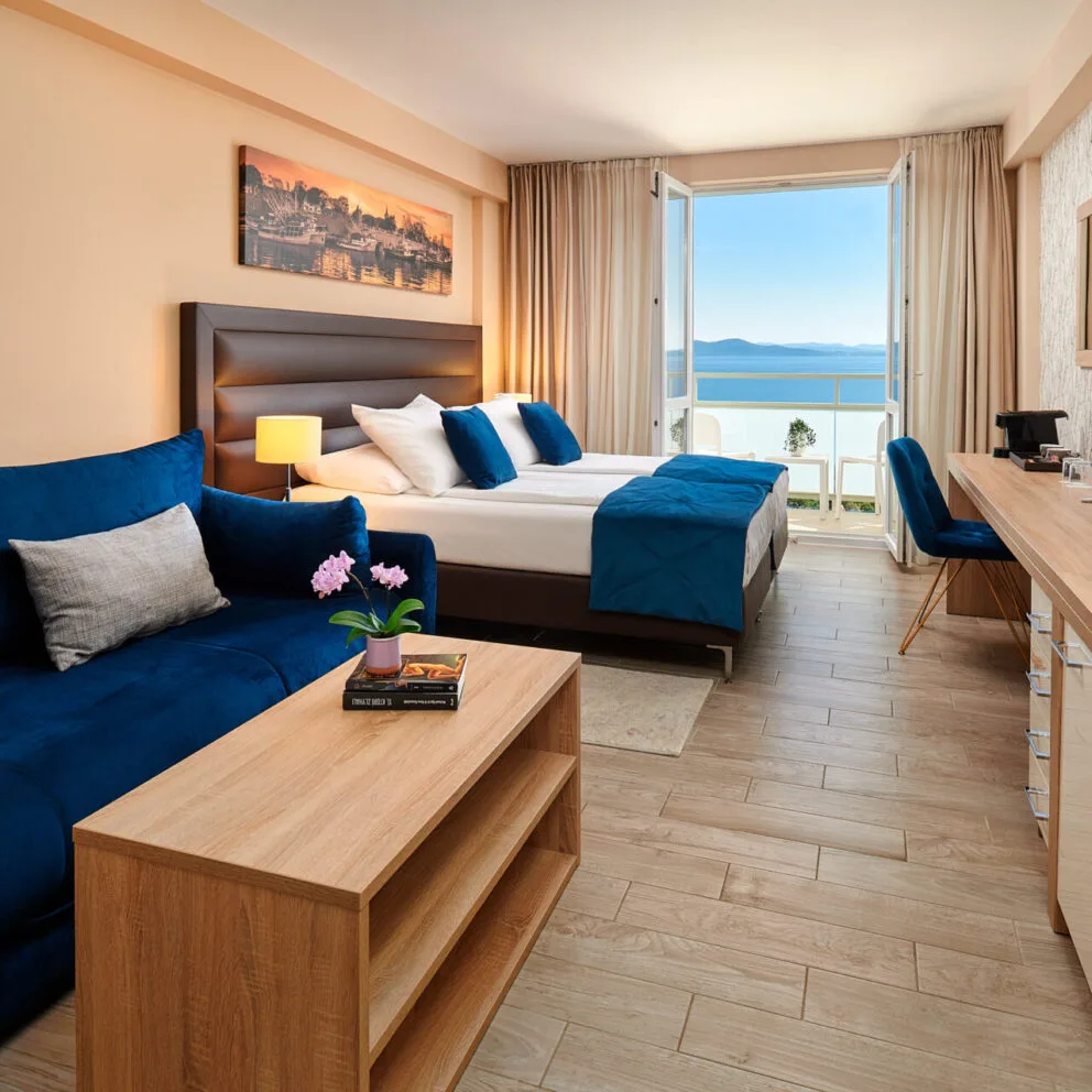 Camera spaziosa con letto, divano blu, scrivania e balcone con vista mare