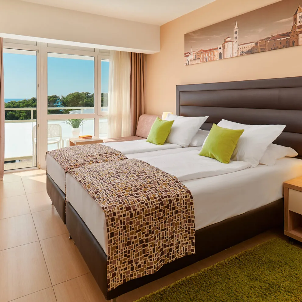 Camera con letto matrimoniale, cuscini verdi e balcone con vista mare