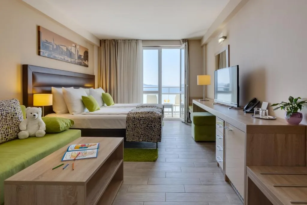 Camera familiare con letto, divano verde, scrivania e balcone con vista mare