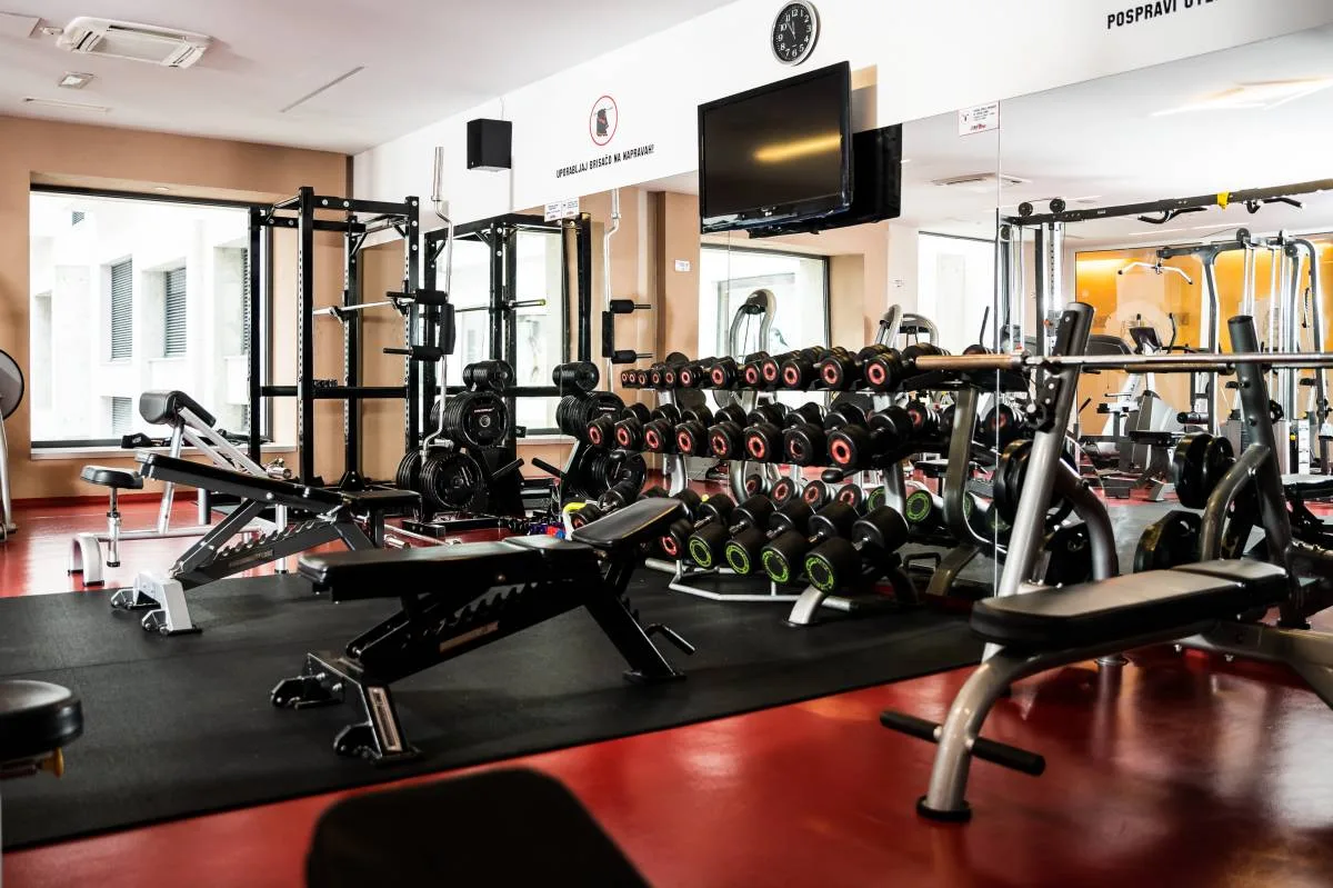 Sala fitness attrezzata con pesi liberi, macchinari e pavimento rosso