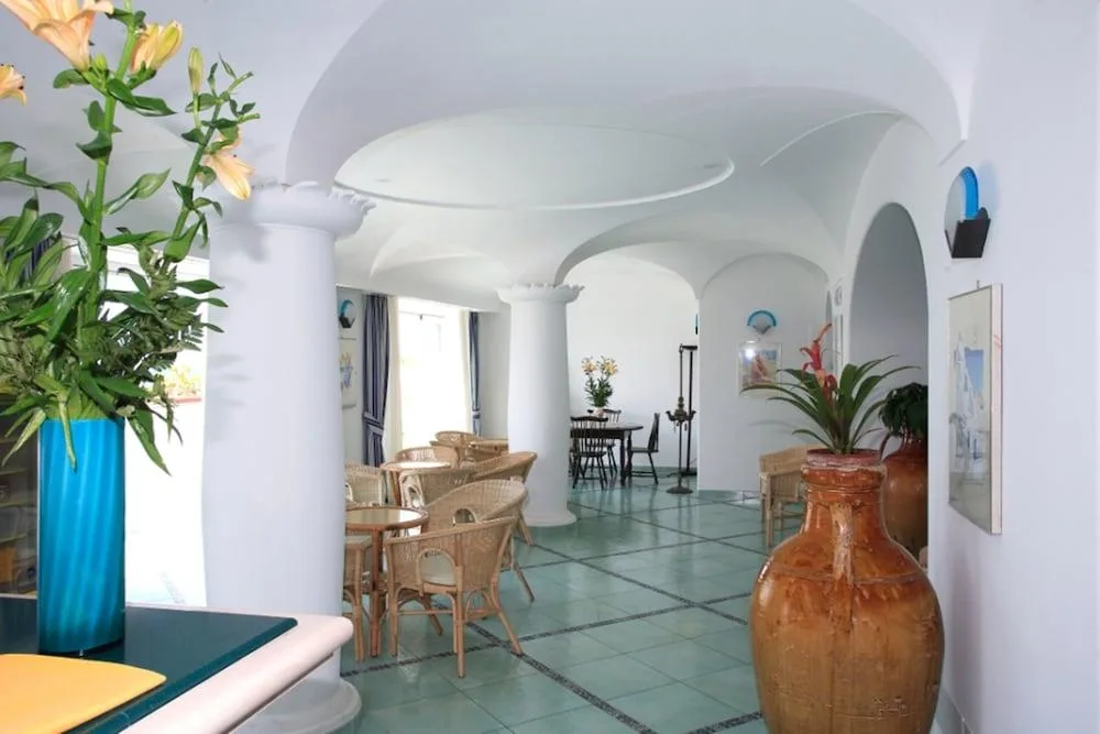 Sala comune dell'hotel con colonne bianche, tavolini in vimini e pavimento in maiolica verde