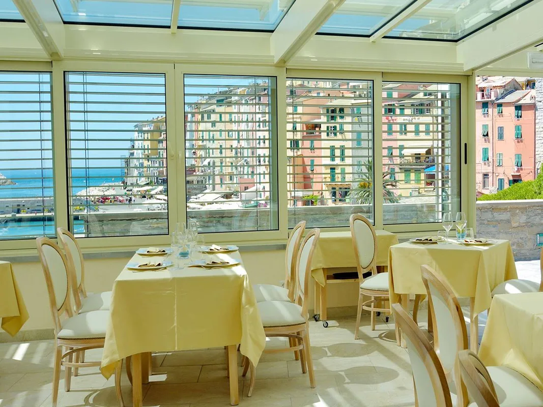 Sala ristorante luminosa con tavoli apparecchiati e veranda affacciata sulle case colorate