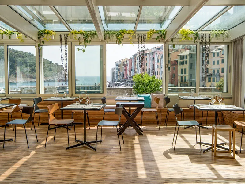 Ristorante con veranda in legno, piante verdi e ampie vetrate con vista sul borgo marino