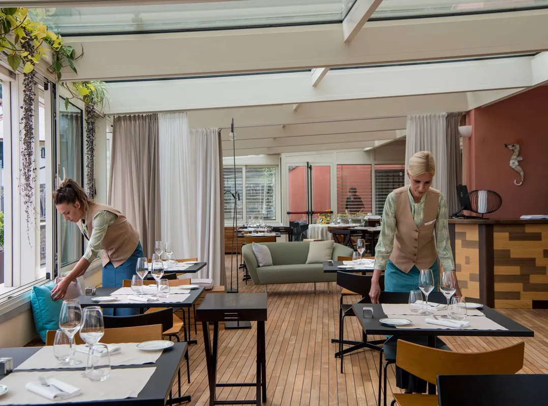 Cameriere che apparecchia i tavoli in un ristorante elegante con veranda e divano verde