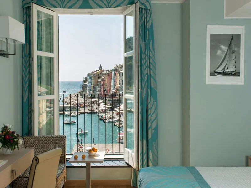 Finestra aperta con vista sul porto di Portovenere dalla camera con tende turchesi
