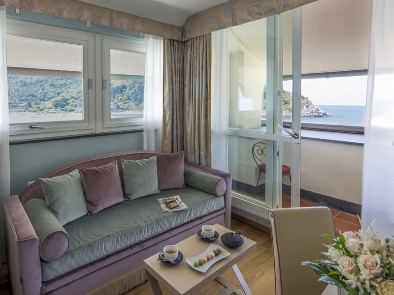 Salottino con divano lilla, poltrone e balcone vista mare con tè servito