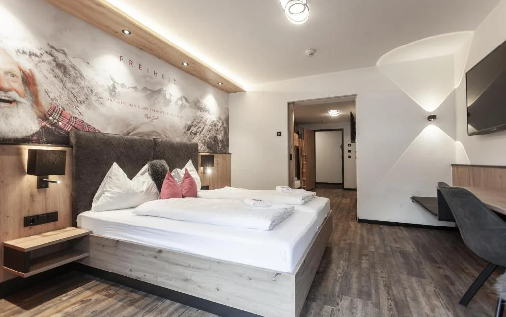 Spaziosa camera moderna con letto matrimoniale, scrivania, TV e decorazione alpina