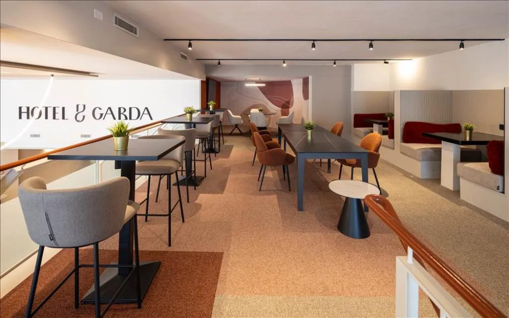 Area lounge dell'Hotel Garda con tavoli, sedie colorate e insegna a parete