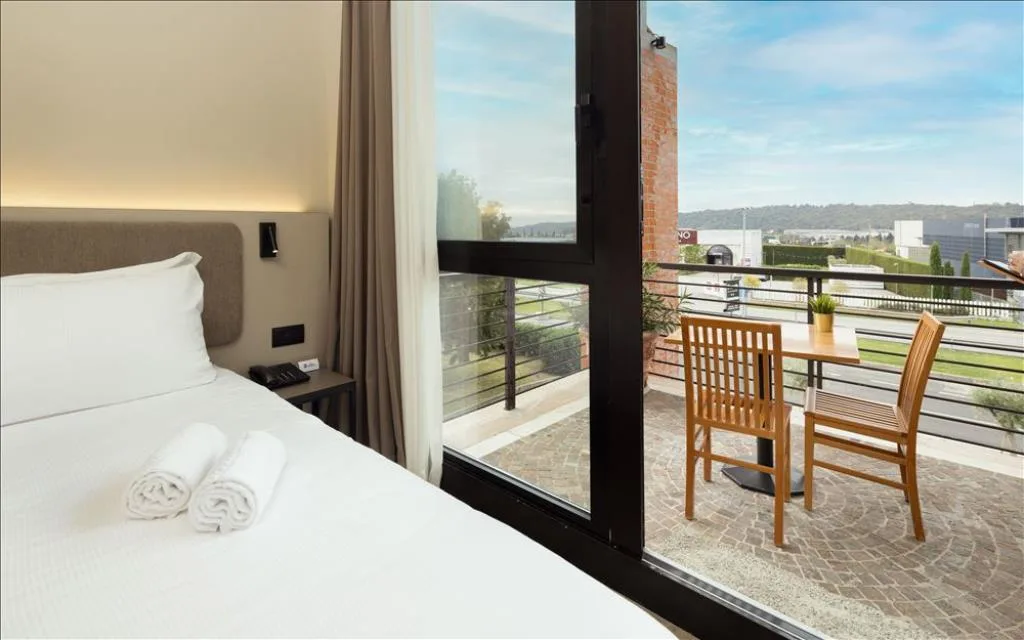 Dettaglio camera con letto e balcone affacciato su paesaggio con tavolo e sedie