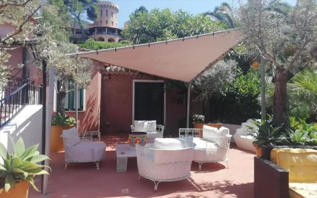 Terrazza esterna con poltrone bianche in ferro battuto, tenda ombreggiante e vegetazione mediterranea