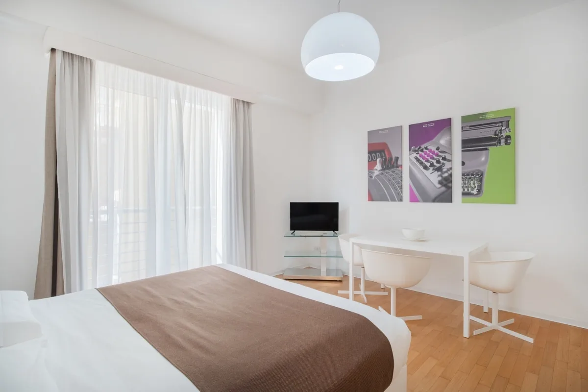 Camera con letto, scrivania bianca con sedie e quadri decorativi colorati