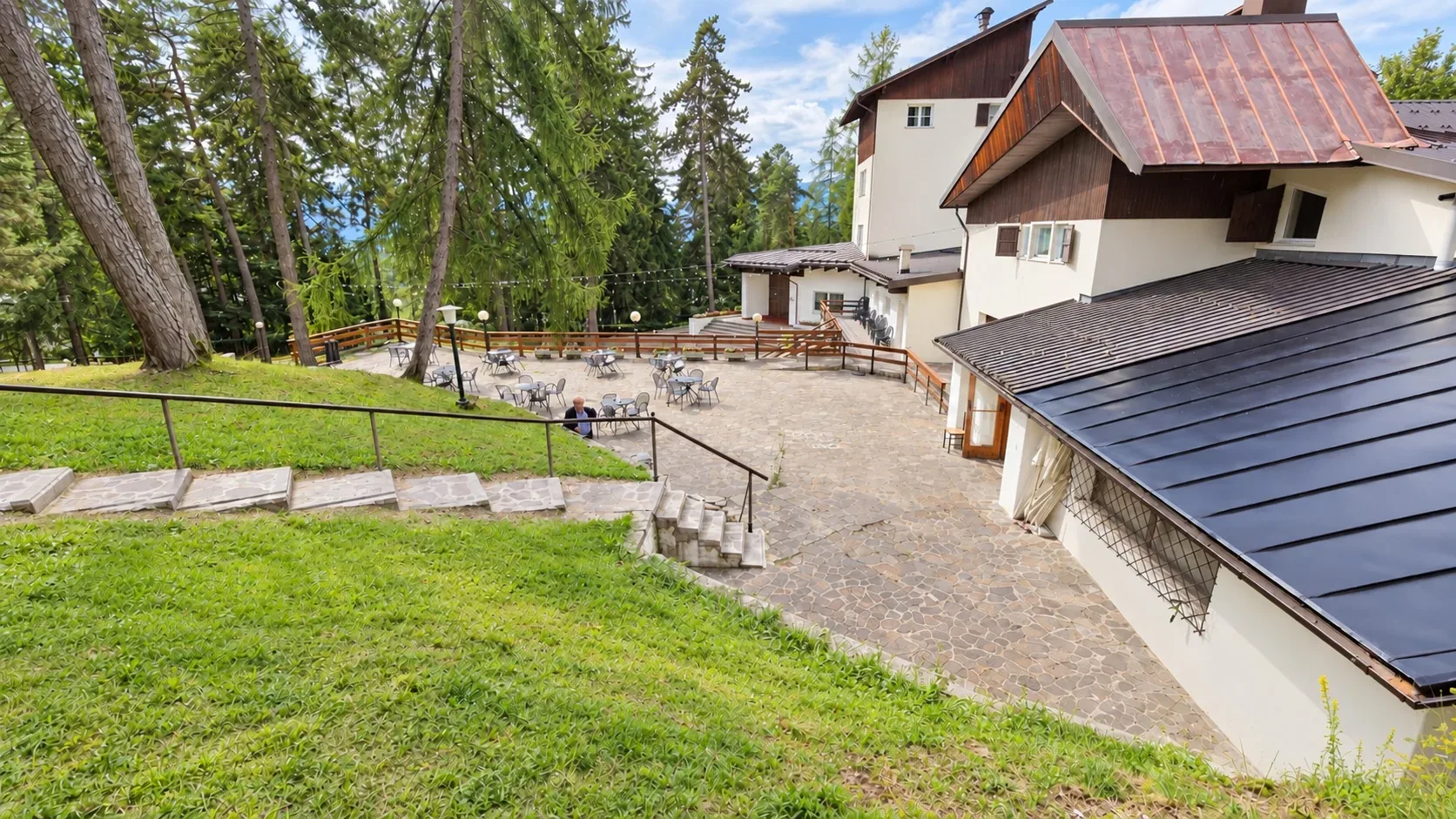Terrazza in pietra con tavolini e tetto in legno dell'hotel tra prati e alberi
