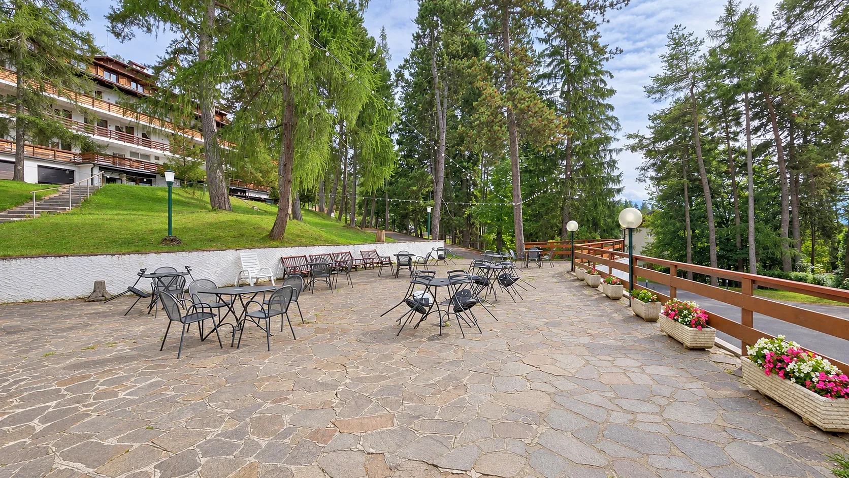 Ampia terrazza pavimentata in pietra con tavoli e sedie e vista sul bosco