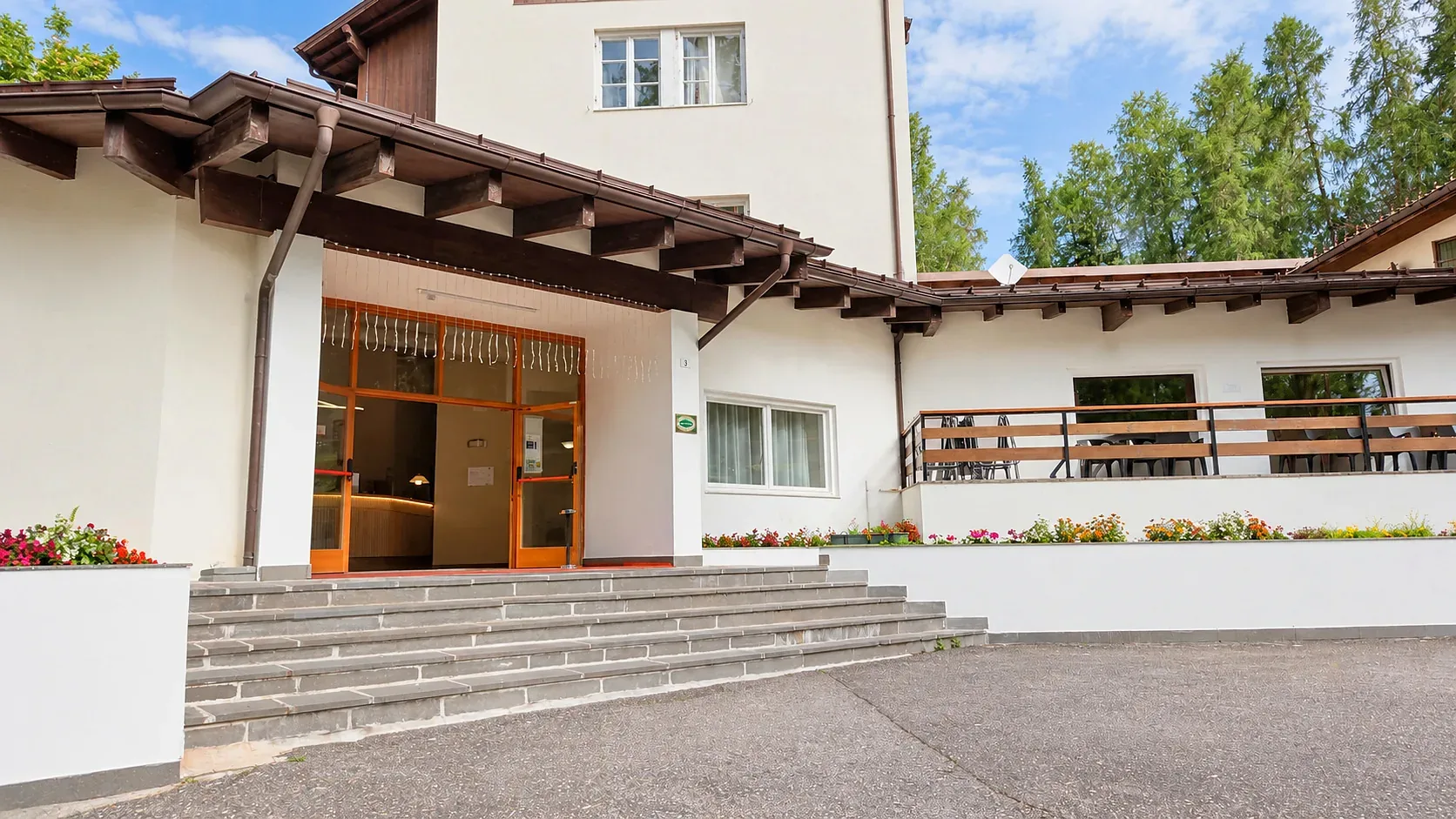 Ingresso principale dell'hotel con portico in legno, scalinata e fiori colorati