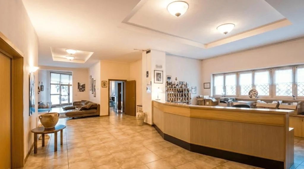 Ampia hall con reception in legno, divani in pelle e pavimento in piastrelle