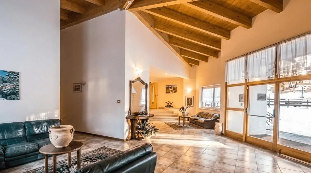 Sala soggiorno luminosa con soffitto in travi di legno, divani in pelle e grandi vetrate