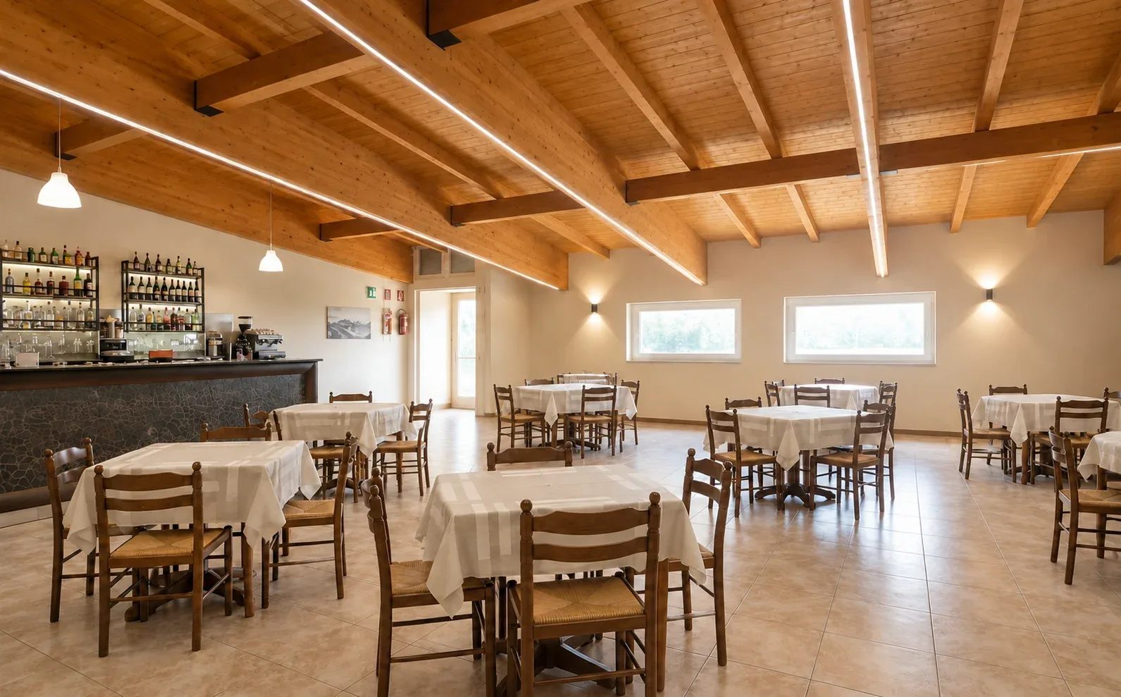 Sala ristorante con soffitto in travi di legno, bar e tavoli apparecchiati