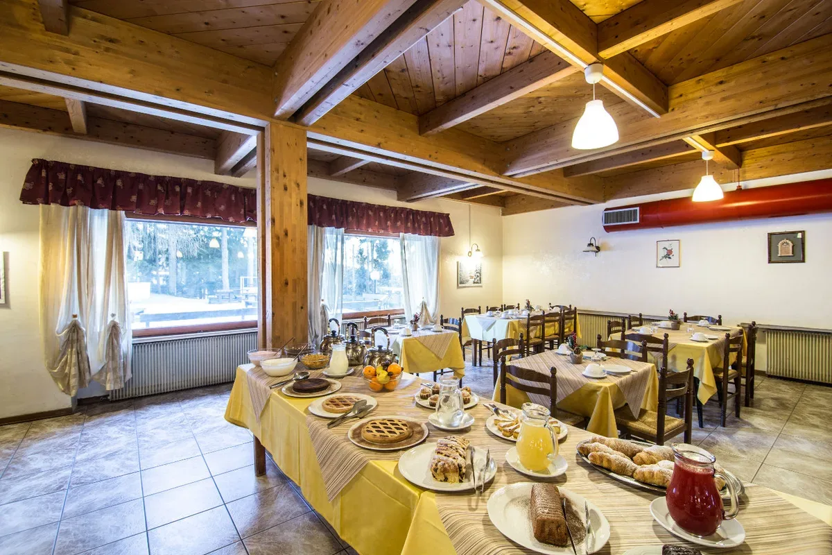 Sala colazione con tavoli apparecchiati e ricco buffet di dolci e frutta