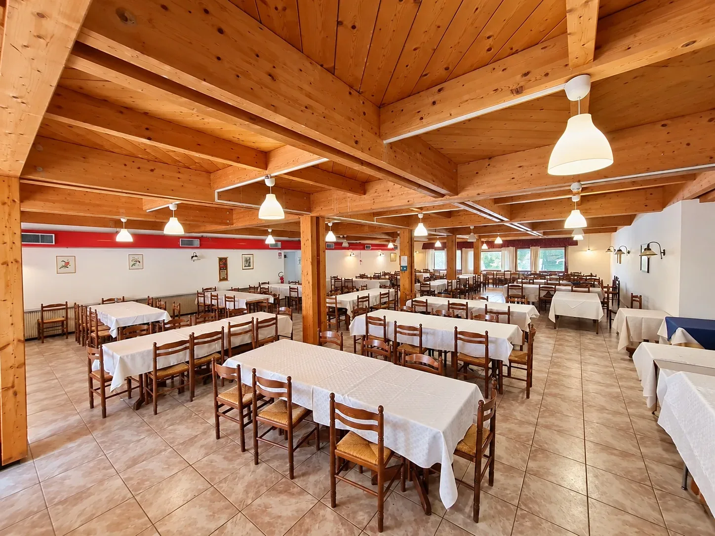 Grande sala ristorante con pilastri in legno, tavoli bianchi e sedie in legno