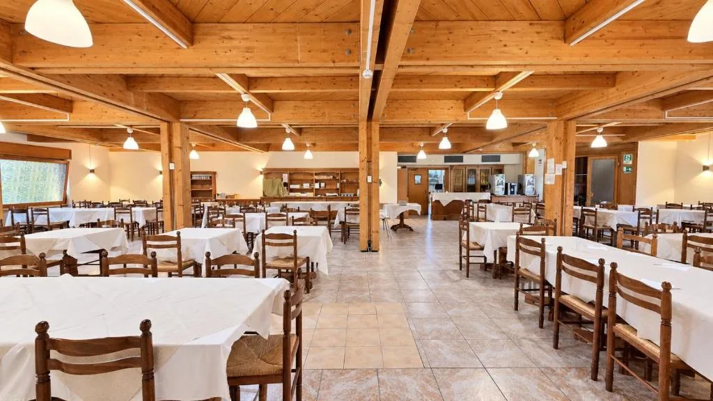Ampia sala da pranzo con soffitto in travi di legno e numerosi tavoli apparecchiati