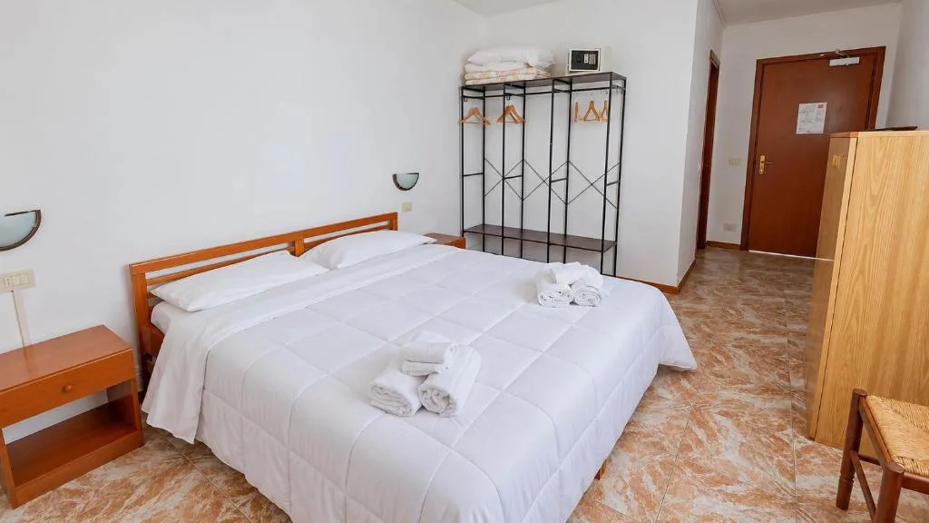 Camera matrimoniale con letto bianco, appendiabiti a vista e pavimento in marmo