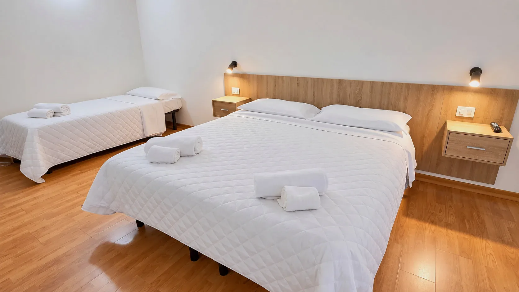 Camera tripla moderna con letti bianchi, testiera in legno e parquet